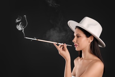 Photo of Woman using long cigarette holder for smoking on black background