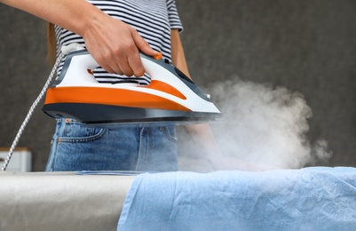 Young woman ironing clothes on board at home, closeup