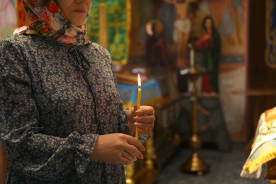 Mature woman holding candle in church, closeup. Space for text