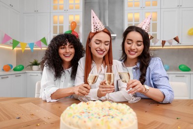 Happy young women clinking glasses of sparkling wine at birthday party in kitchen
