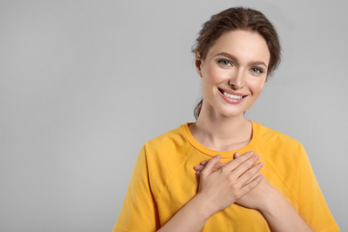 Beautiful grateful woman with hands on chest against light grey background. Space for text