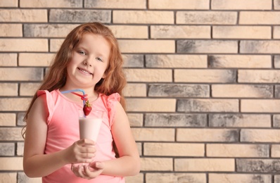 Photo of Little girl with glass of delicious milk shake on brick wall background