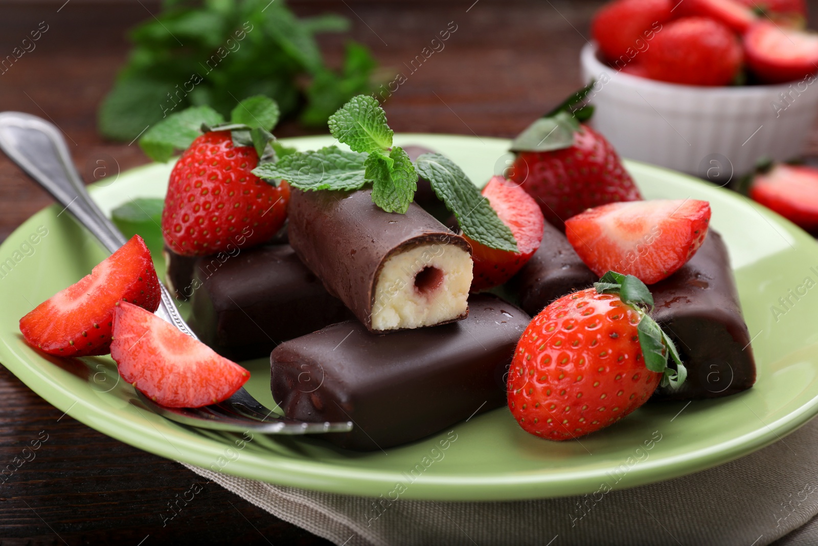 Photo of Delicious glazed curd snacks with fresh strawberries and mint on wooden table, closeup