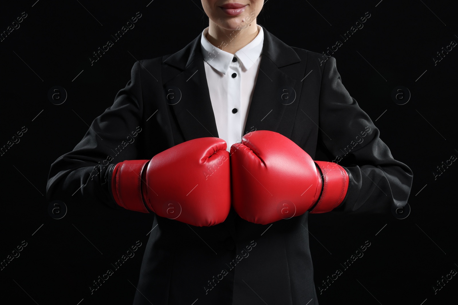 Photo of Businesswoman in suit wearing boxing gloves on black background, closeup