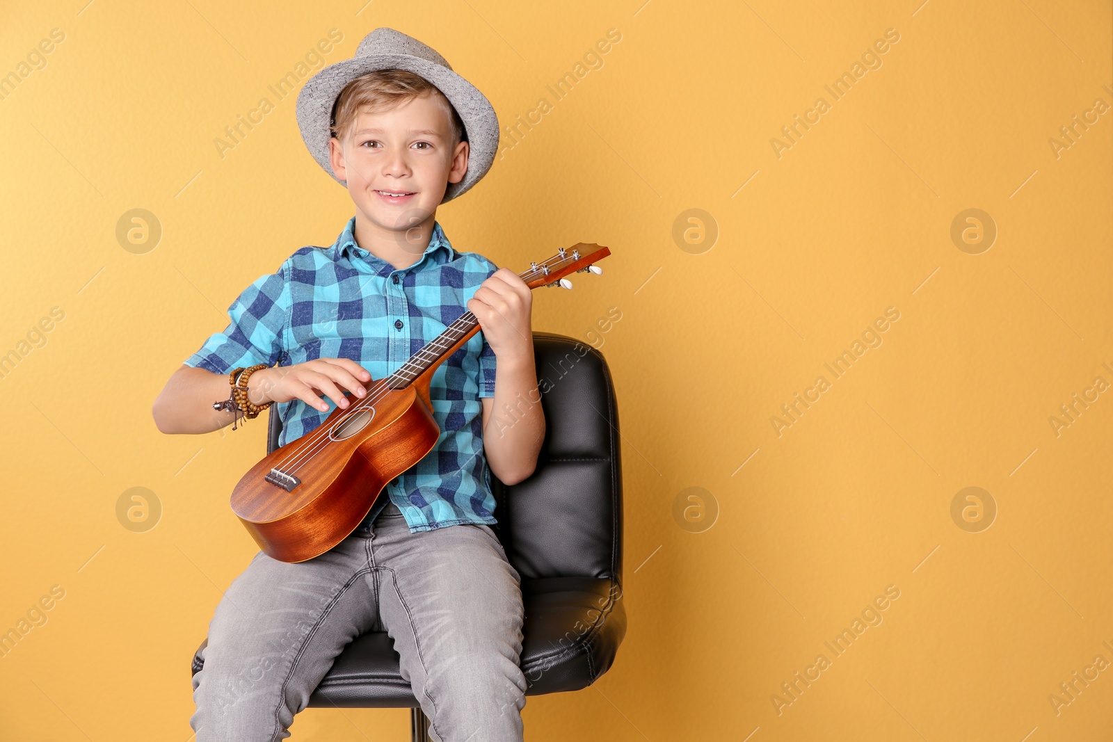 Photo of Little boy sitting on chair and playing guitar against color background. Space for text