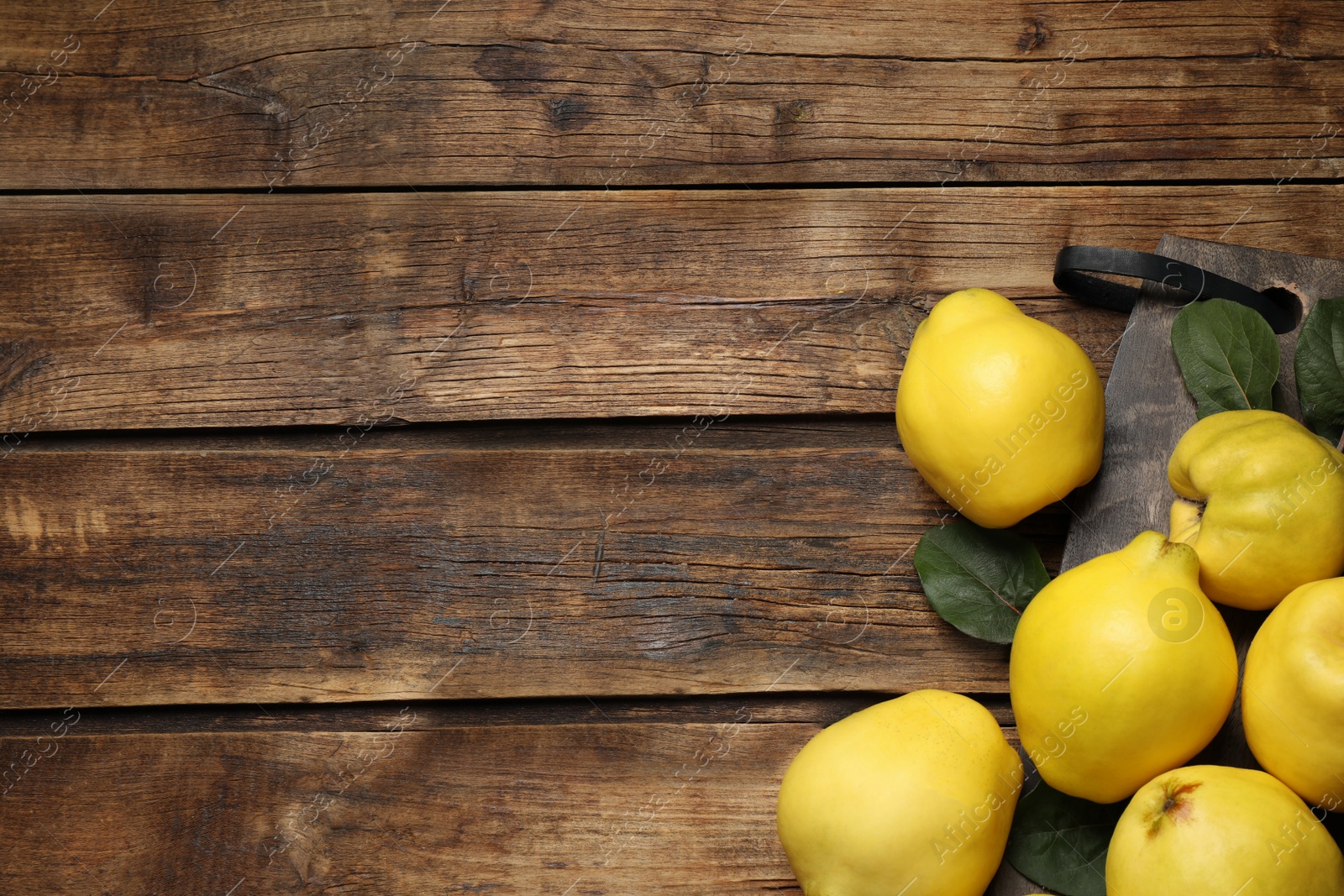 Photo of Fresh ripe organic quinces with leaves on wooden table, flat lay. Space for text