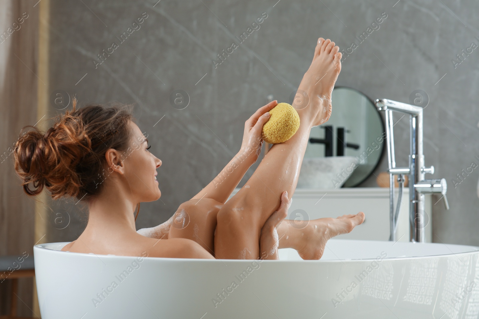 Photo of Beautiful woman with sponge taking bath indoors