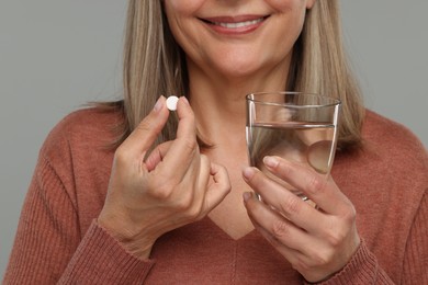 Senior woman with glass of water and pill on grey background, closeup