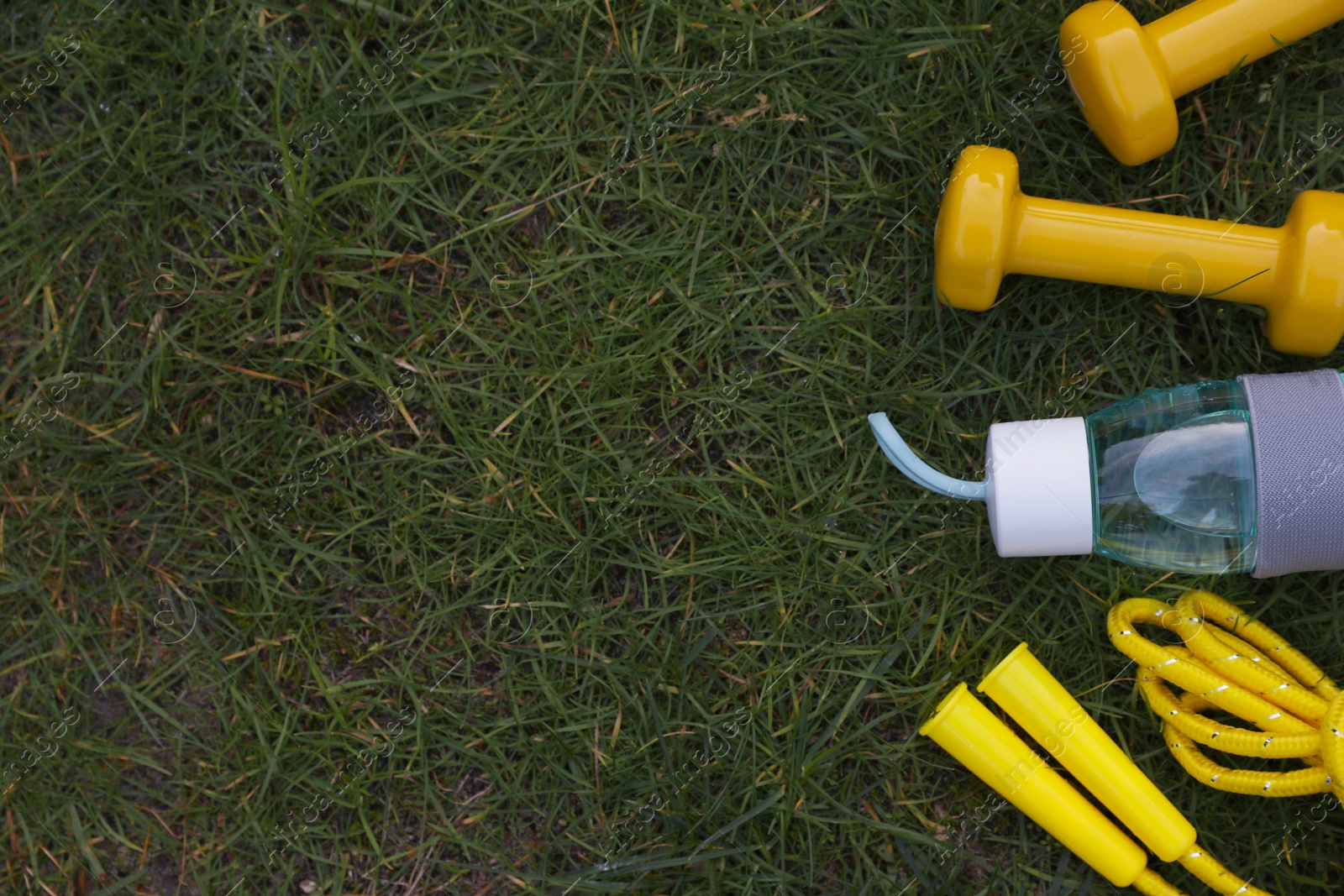 Photo of Skipping rope, dumbbells and bottle of water on grass, flat lay with space for text. Morning exercise