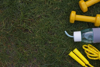 Photo of Skipping rope, dumbbells and bottle of water on grass, flat lay with space for text. Morning exercise