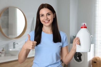 Woman holding fabric softener and showing thumbs up in bathroom