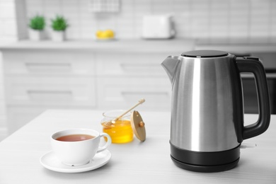Photo of Modern electric kettle, cup of tea and honey on wooden table in kitchen