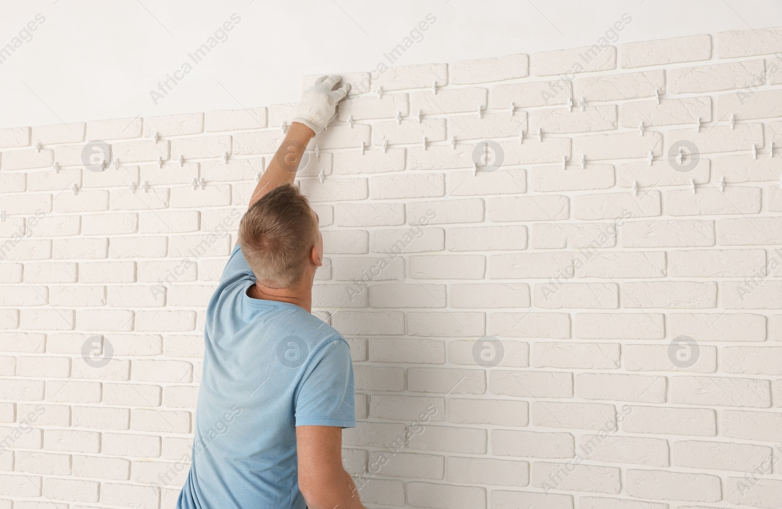 Photo of Professional builder installing new white decorative bricks on wall, back view