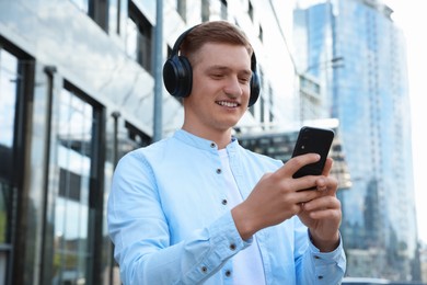 Photo of Smiling man in headphones using smartphone outdoors