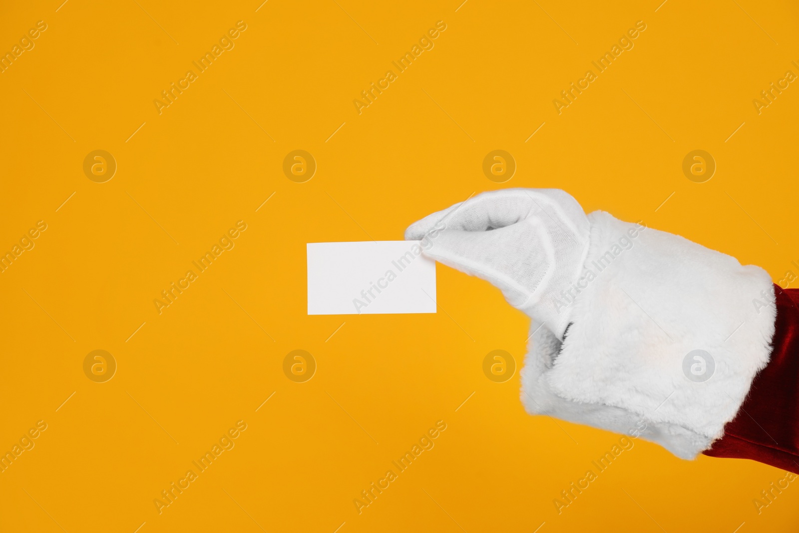 Photo of Santa Claus holding blank card on yellow background, closeup of hand. Space for text