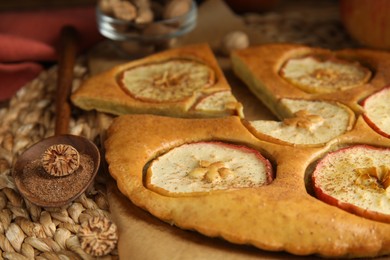 Photo of Nutmeg powder, seed and tasty apple pie on wicker mat, closeup