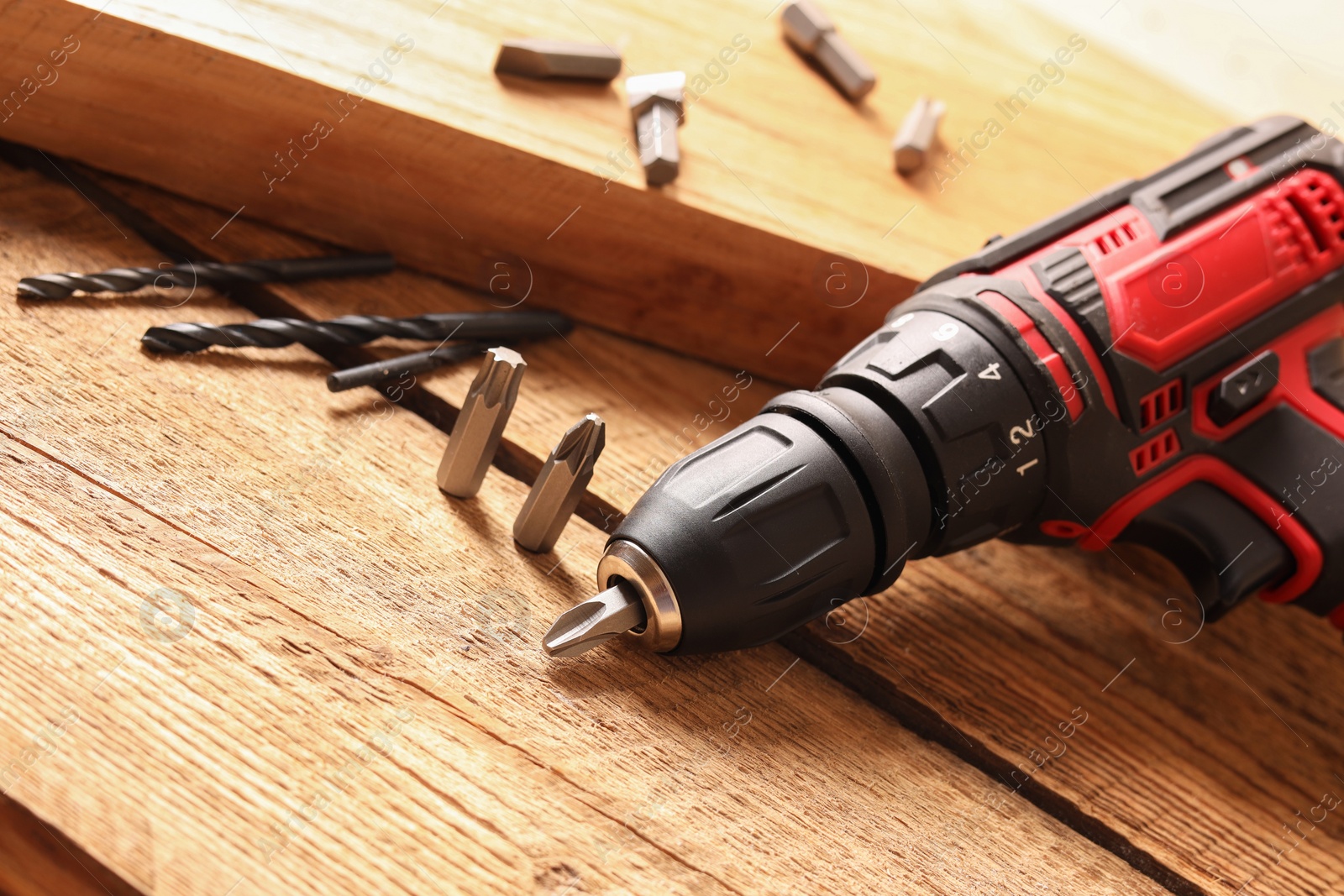 Photo of Electric screwdriver with bits and drills on wooden table, closeup