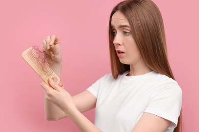 Photo of Upset woman untangling her lost hair from comb on pink background. Alopecia problem