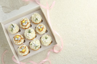 Photo of Tasty Easter cupcakes with vanilla cream in box and pink ribbon on beige table, flat lay. Space for text