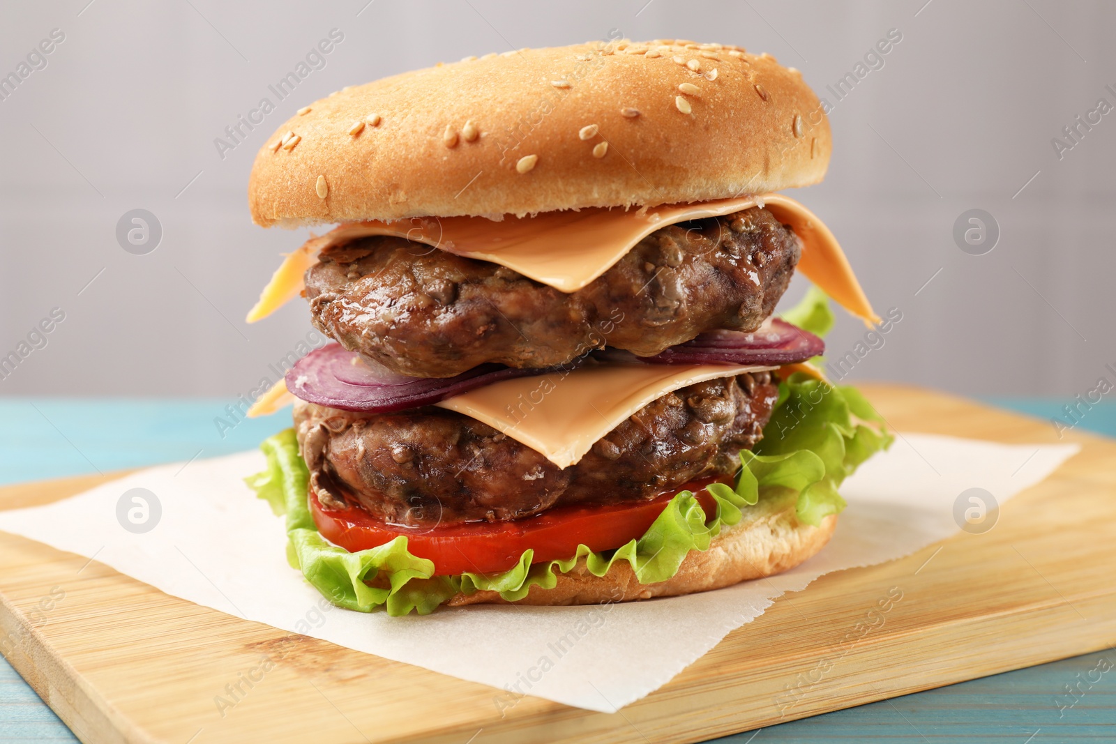 Photo of Tasty hamburger with patties, cheese and vegetables on table