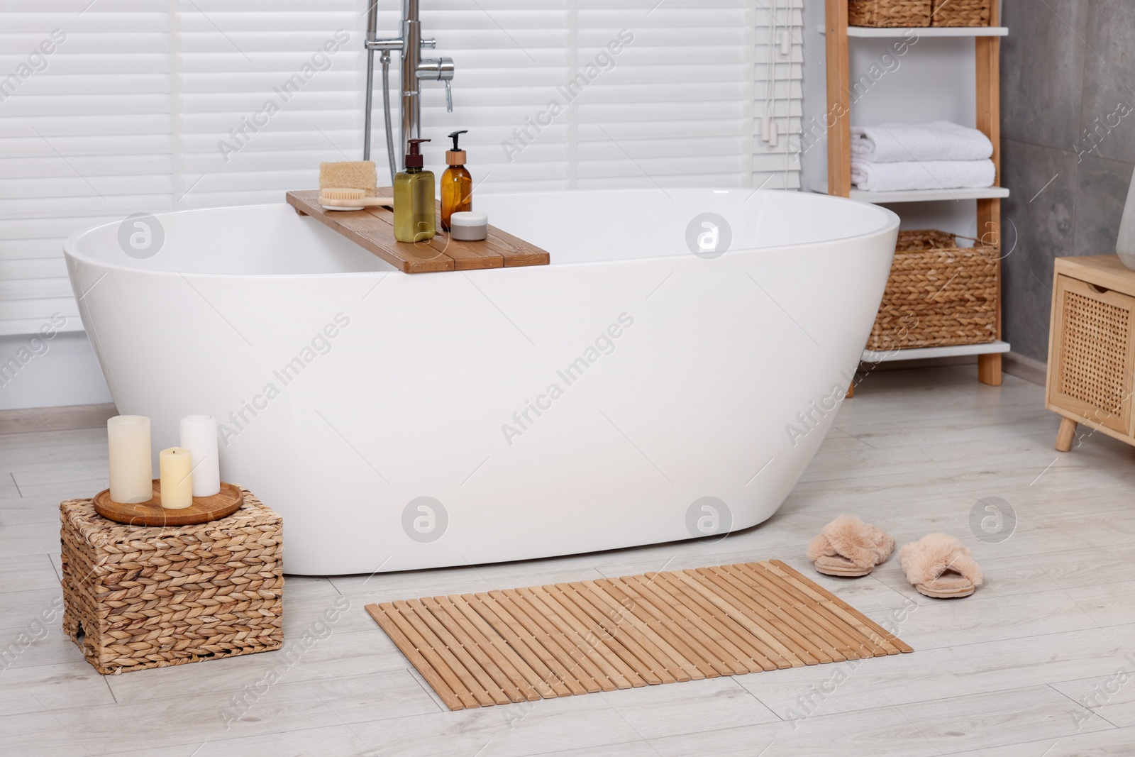 Photo of Stylish bathroom interior with bamboo bath mat and white tub