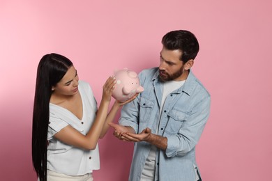 Photo of Couple with ceramic piggy bank on pale pink background