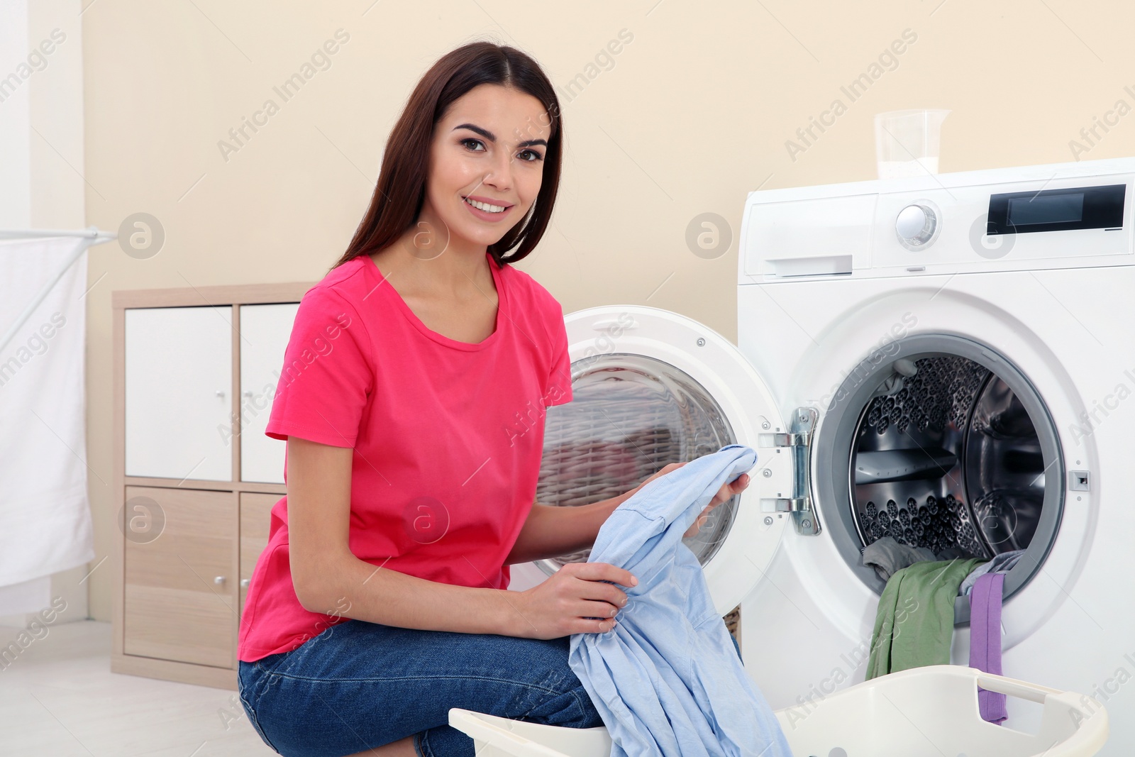 Photo of Young woman taking laundry out of washing machine at home