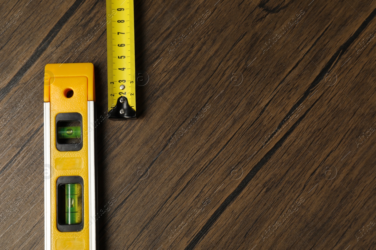 Photo of Building level and tape measure on wooden table, top view. Space for text