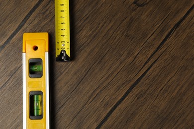 Building level and tape measure on wooden table, top view. Space for text