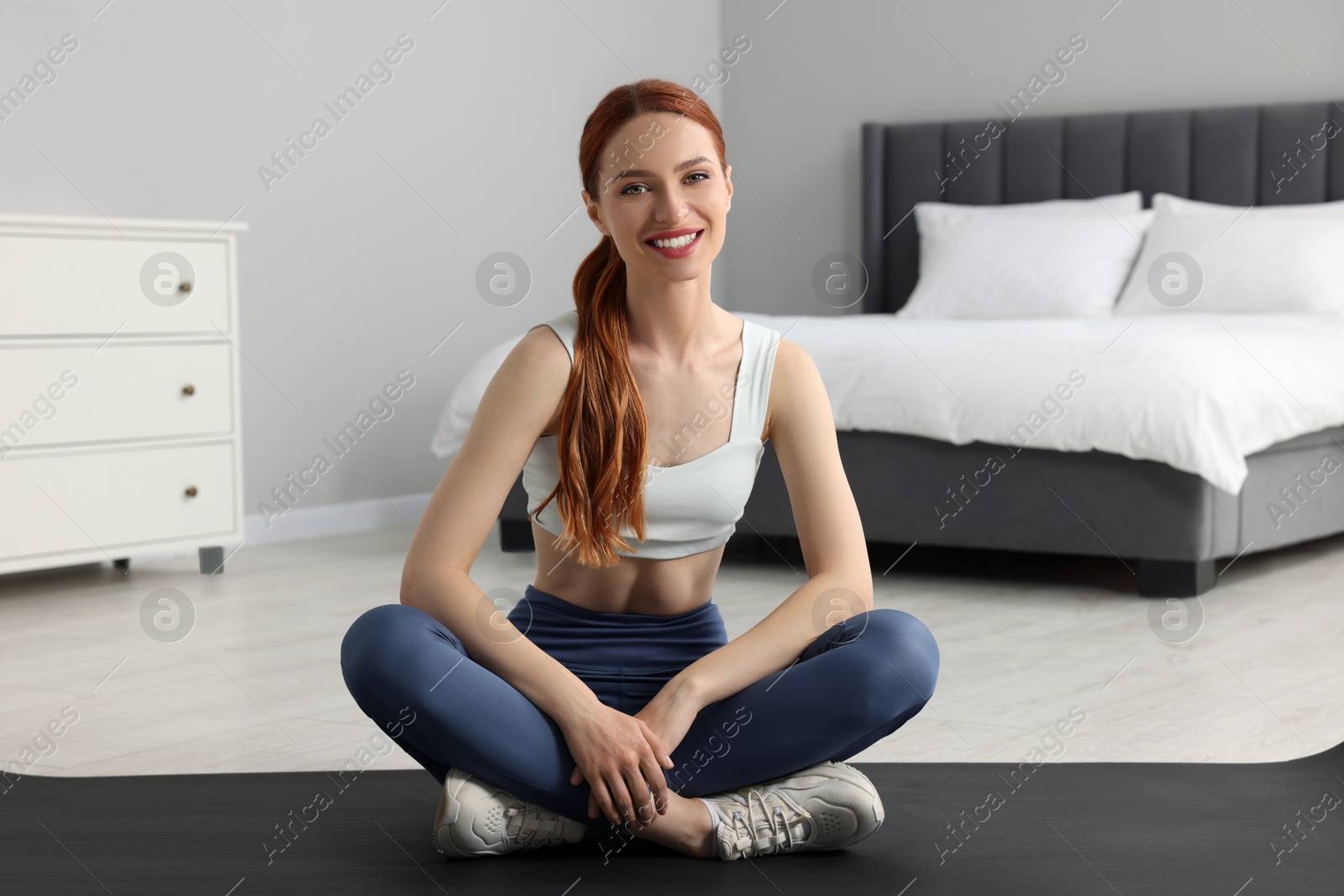 Photo of Young woman in sportswear sitting on fitness mat in bedroom