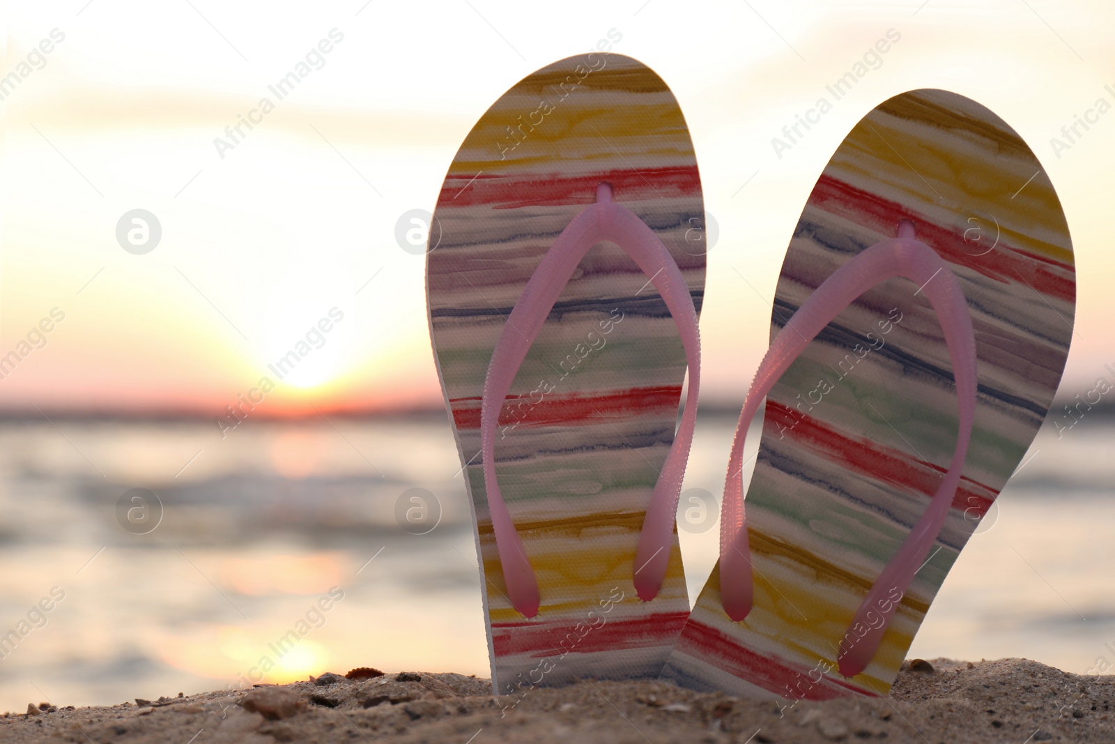 Photo of Stylish flip flops on sand near sea, closeup. Beach accessories
