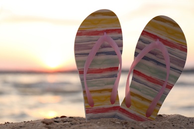 Stylish flip flops on sand near sea, closeup. Beach accessories