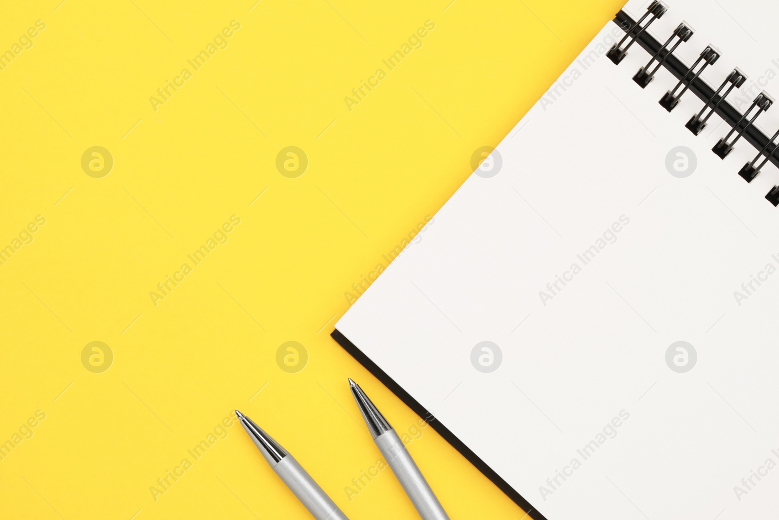 Photo of Notebook and pens on yellow background, flat lay. Space for text