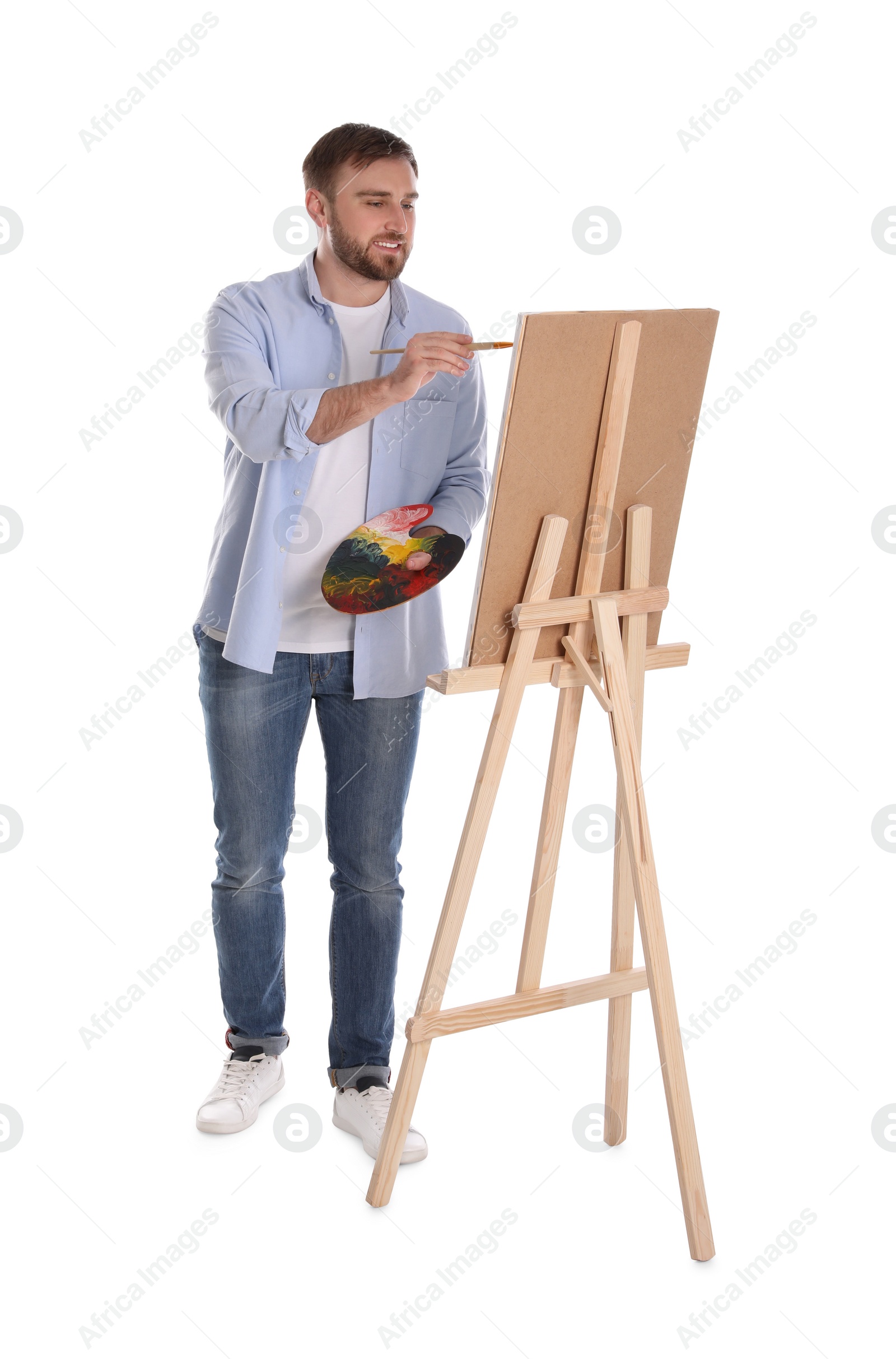 Photo of Man painting with brush on easel against white background. Young artist