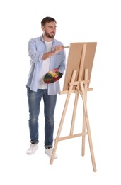 Man painting with brush on easel against white background. Young artist