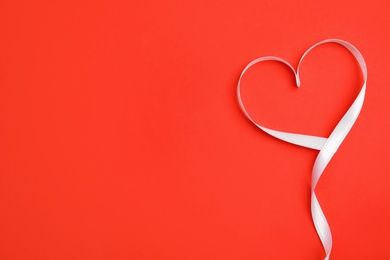 Heart made of white ribbon on red background, top view with space for text. Valentine's day celebration