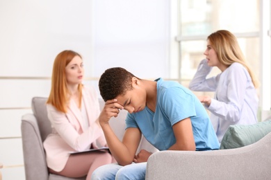 Photo of Young female psychologist working with teenage boy and his mother in office