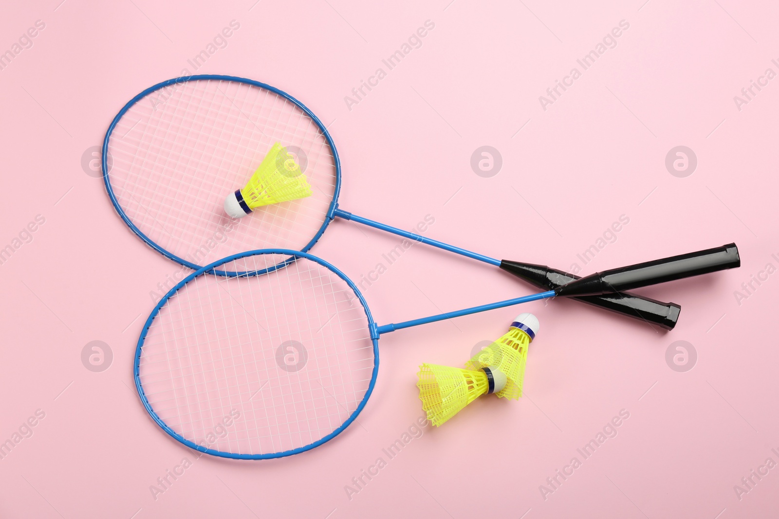 Photo of Rackets and shuttlecocks on pink background, flat lay. Badminton equipment
