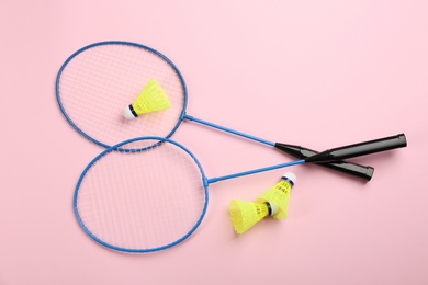 Photo of Rackets and shuttlecocks on pink background, flat lay. Badminton equipment
