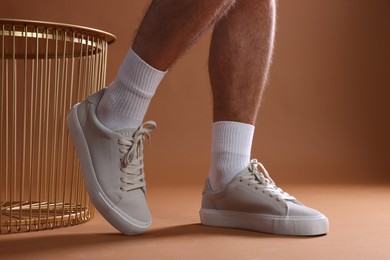 Photo of Man wearing stylish sneakers on brown background, closeup