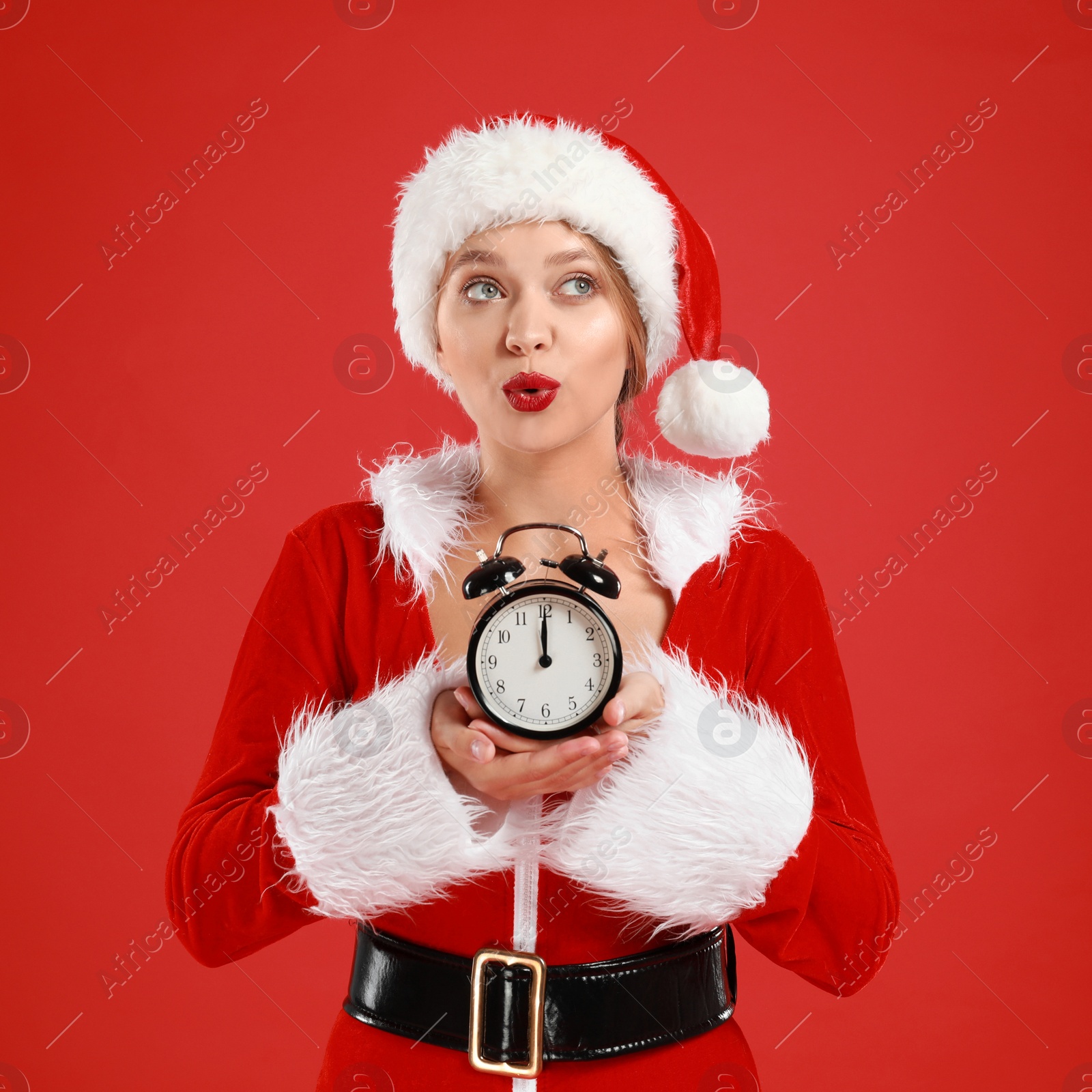 Photo of Beautiful Santa girl with alarm clock on red background. Christmas eve