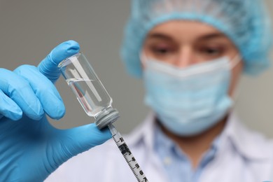 Doctor filling syringe with medication from glass vial on grey background, selective focus