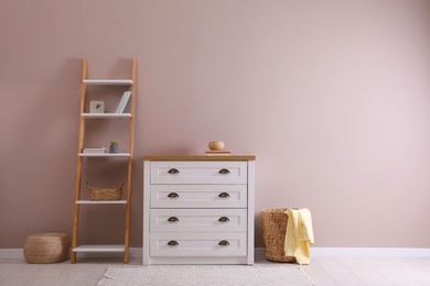 Photo of Elegant room interior with stylish chest of drawers, shelving unit and wicker basket. Space for text
