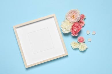 Photo of Empty photo frame and beautiful flowers on light blue background, flat lay. Space for design