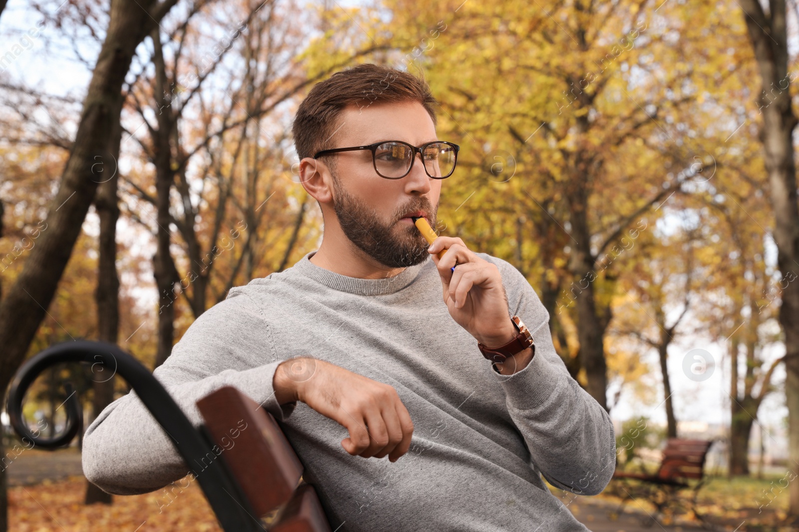 Photo of Handsome young man using disposable electronic cigarette in park on autumn day