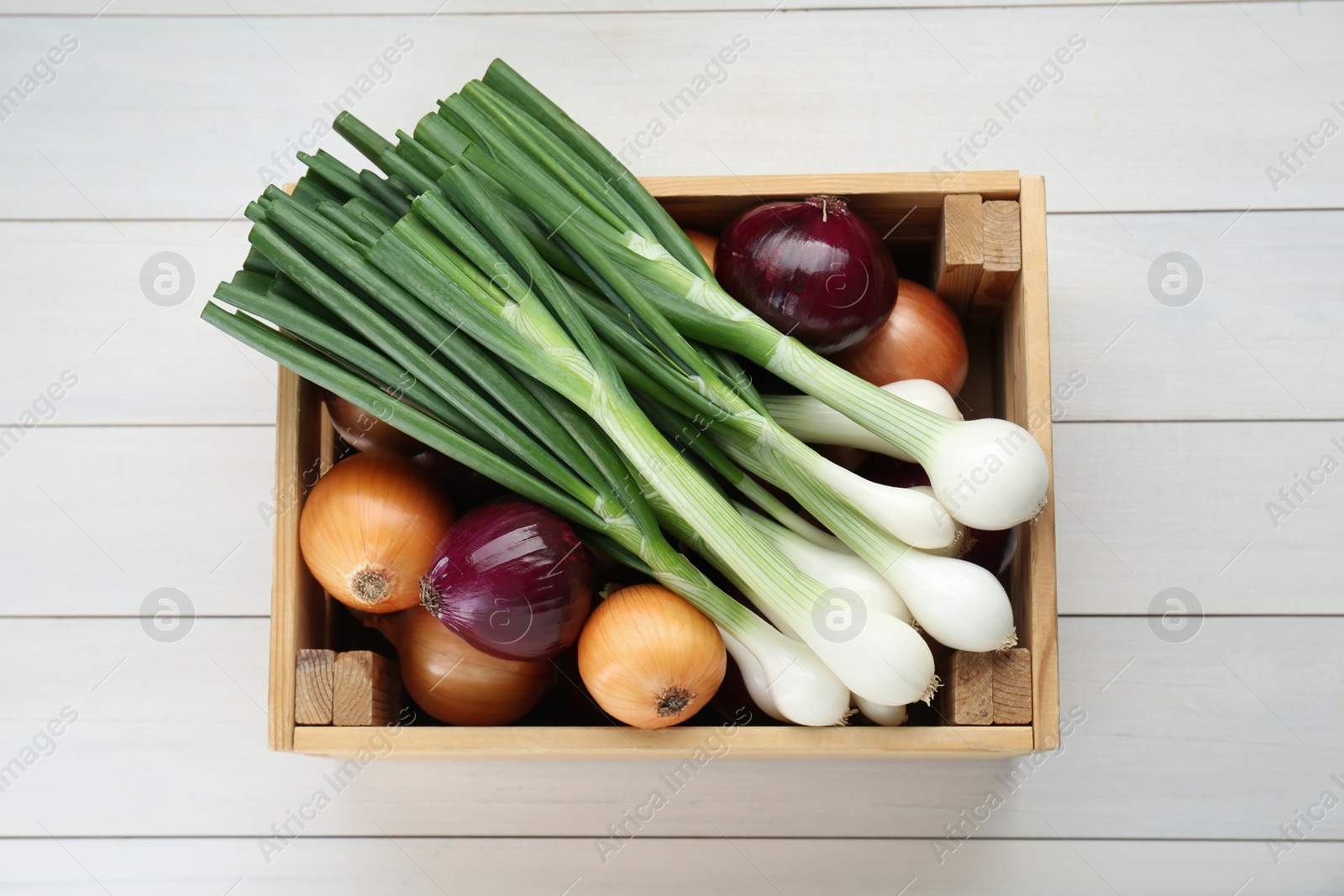 Photo of Crate with different kinds of onions on white wooden table, top view