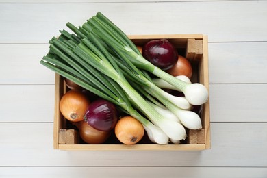 Crate with different kinds of onions on white wooden table, top view