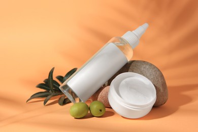 Photo of Cosmetic products and olives on orange background