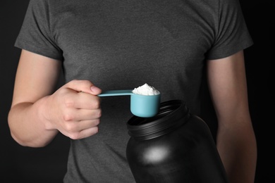 Photo of Man with scoop and jar of protein powder on black background, closeup