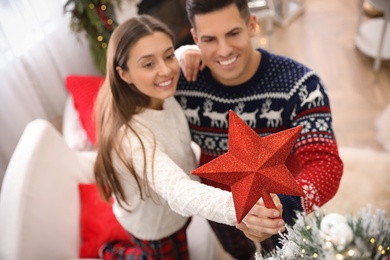Couple decorating Christmas tree indoors, focus on star topper